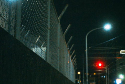 夜間の街灯と信号機が照らすフェンス沿いの道路