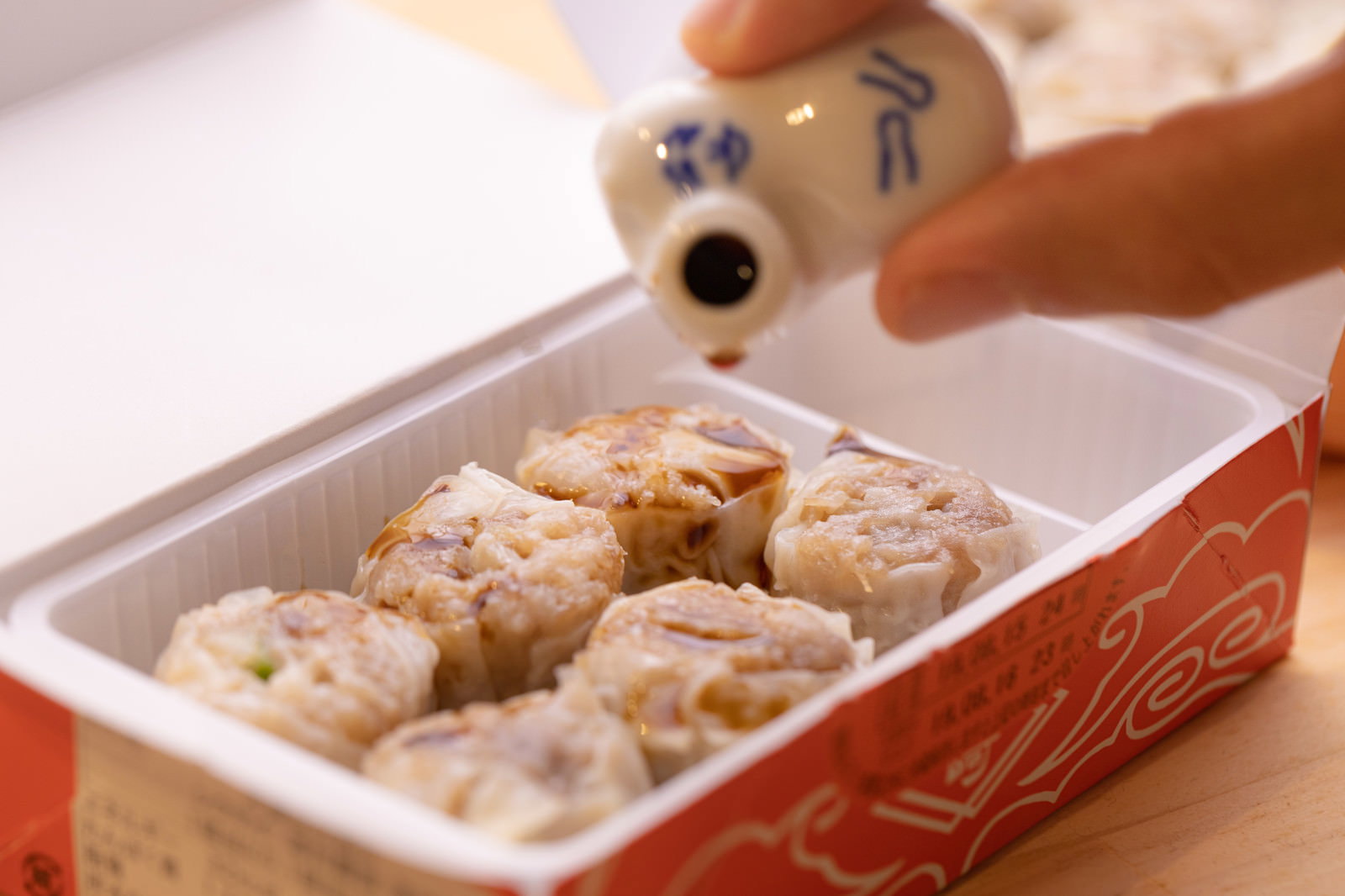 蒸籠に入った焼売にしょう油差しでしょう油をかけている様子