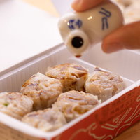 蒸籠の焼売にしょう油をかけて食べるスタイルの写真