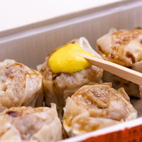 シウマイに黄色いからしをつける木の箸と中華料理の定番の写真