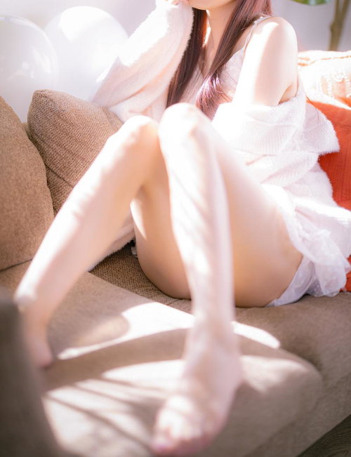 朝の陽だまりの中、ソファーに座る白いシャツの女性の写真
