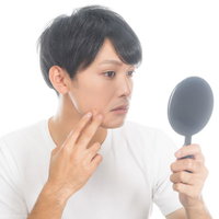 手鏡で頬の肌をチェックする男性の写真
