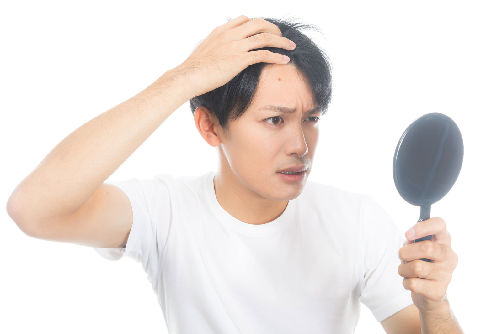 手鏡を持っておでこのニキビを確認している白いTシャツの男性［モデル：完伍］