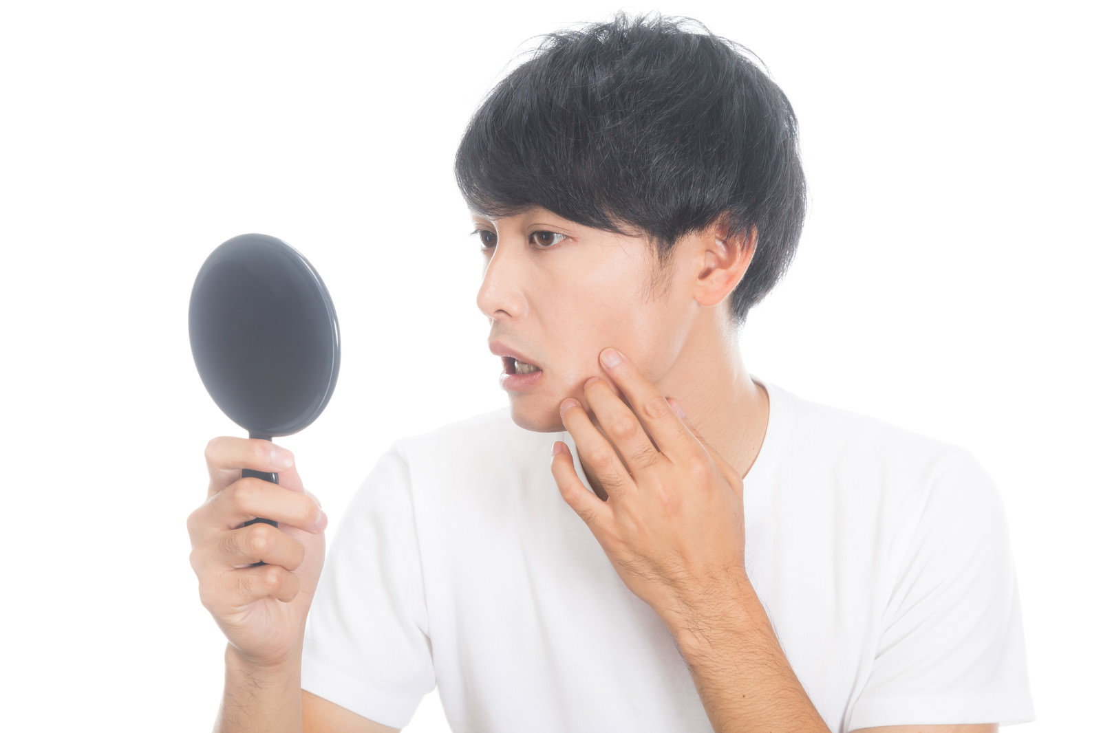 白いシャツを着た男性が手鏡を見ながら頬のニキビをチェックしている［モデル：完伍］