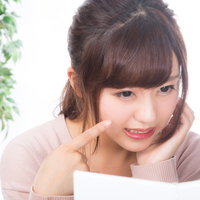 頬のニキビに悩む女性が鏡を見ながら困り顔の写真