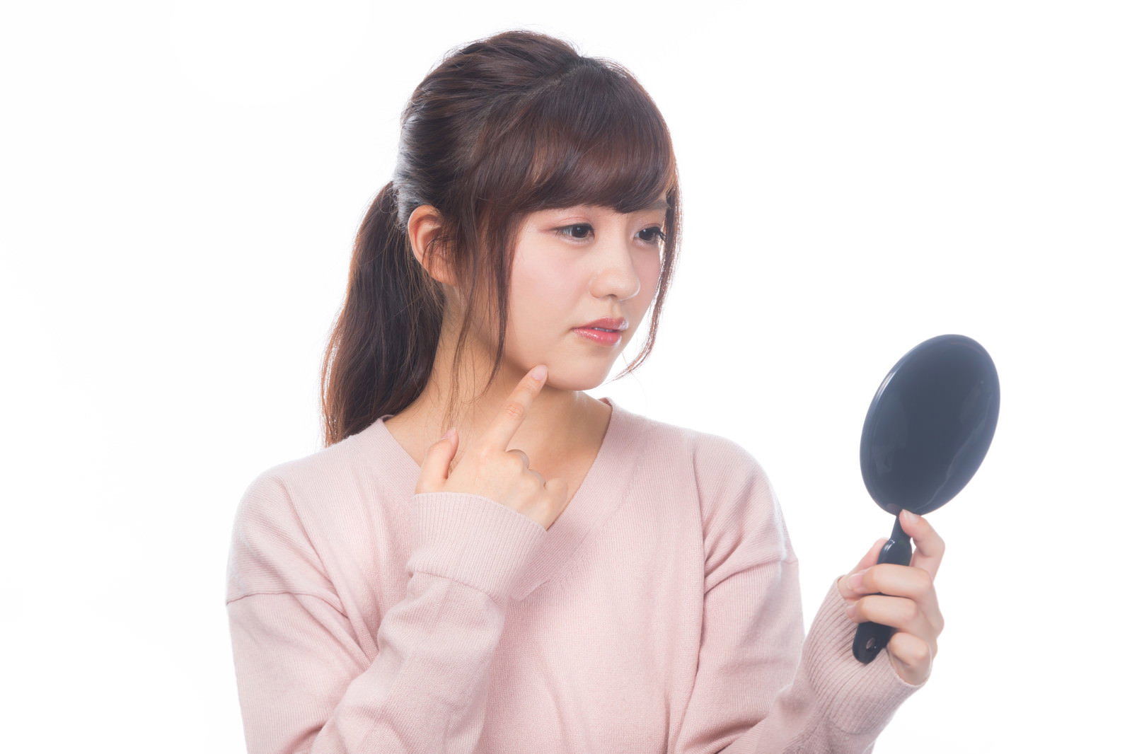 手鏡を持ってニキビを確認している若い女性［モデル：河村友歌］