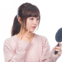手鏡でニキビを確認する若い女性のスキンケアチェックの写真