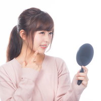 手鏡で吹き出物をチェックする女性のスキンケアの写真