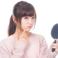 手鏡で肌のニキビをチェックして不満顔の女性の写真