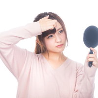 おでこのニキビが気になる手鏡を持つ女性のスキンケアの写真