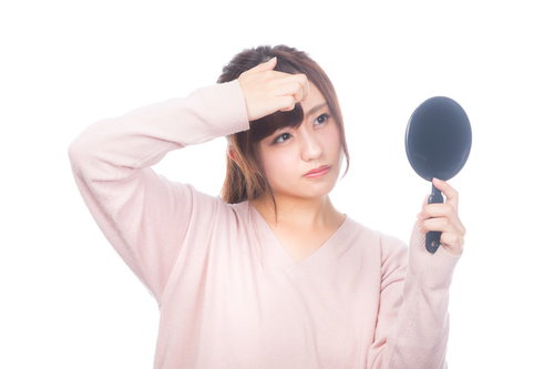 おでこのニキビが気になる手鏡を持つ女性のスキンケア