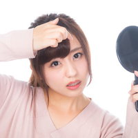 おでこのニキビを気にして手鏡で確認する女性の写真