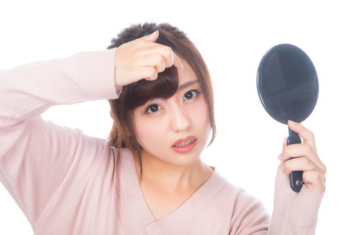 おでこのニキビを気にして手鏡で確認する女性