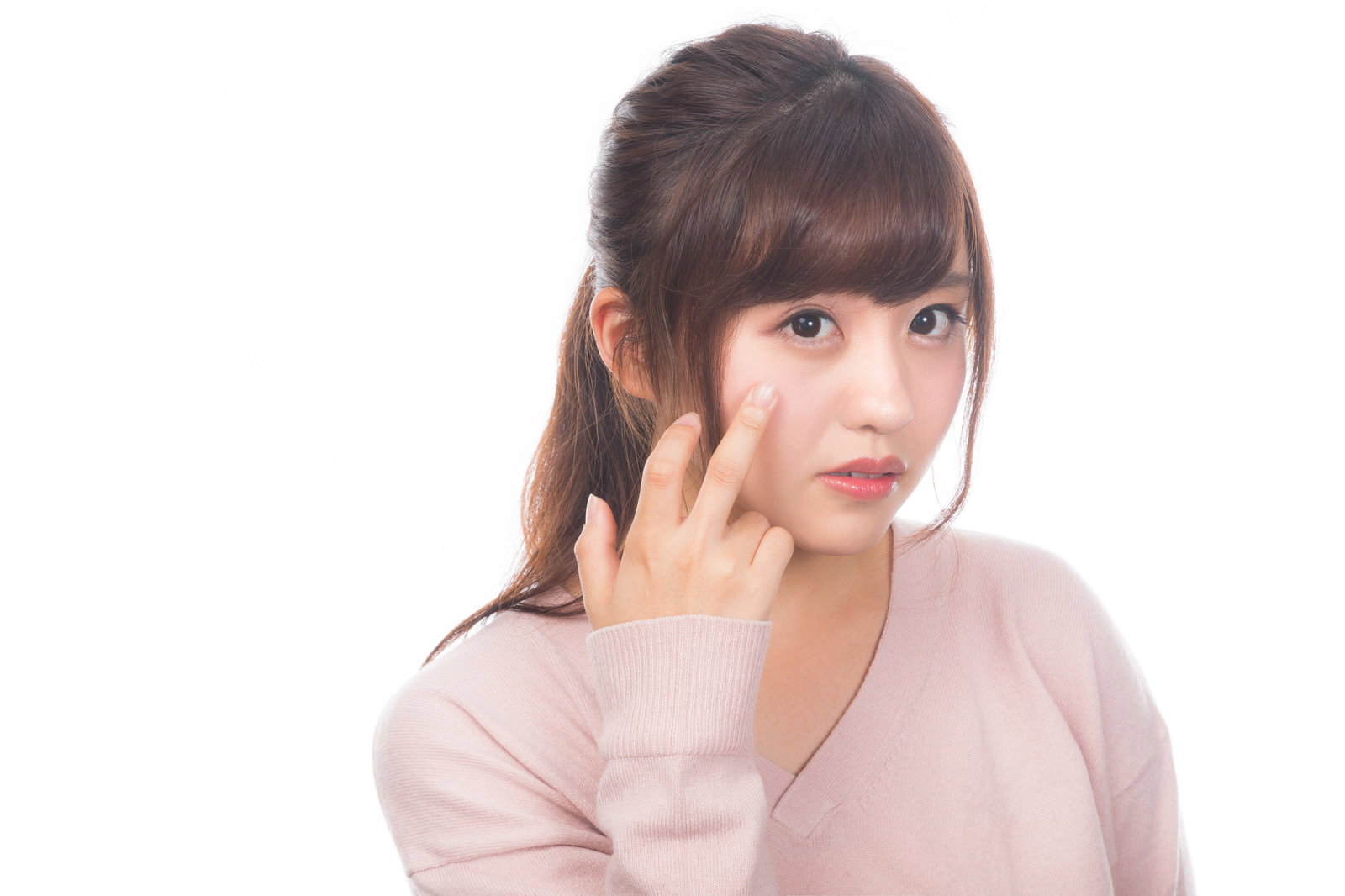 ベージュのトップスを着た女性が片手を頬に当てて肌荒れを気にしている様子［モデル：河村友歌］