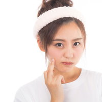 肌の状態を気にして頬に手を当てるニキビ悩みの女性の写真