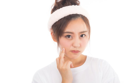 肌の状態を気にして頬に手を当てるニキビ悩みの女性