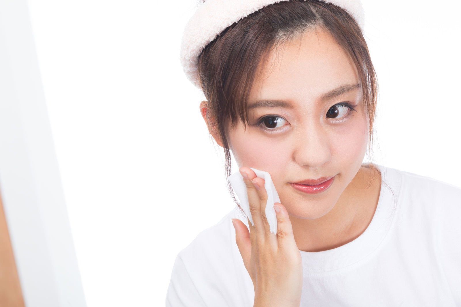 鏡を見ながらコットンでクレンジングをする白いトップスの女性［モデル：河村友歌］