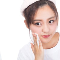 鏡を見ながらコットンでクレンジングする女性の写真