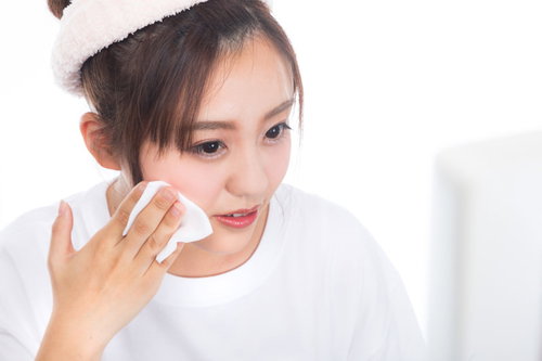 鏡を見ながらコットンでメイクや脂汚れを落とすスキンケアの女性