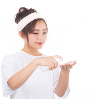 白いヘアバンドをした女性がコットンに化粧水をつけるの写真