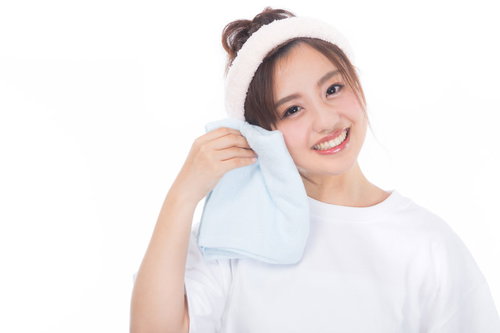 白いタオルを頬にあてるスキンケア中の女性