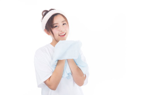 朝に顔を洗った後、白いタオルで顔を拭く女性