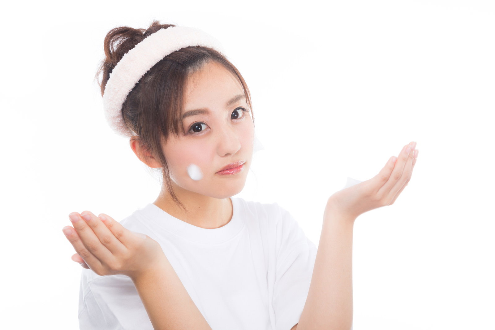 白いヘアバンドをした女性が両手でクレンジングの泡を頬につけている様子［モデル：河村友歌］