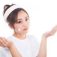 白いヘアバンドをした女性が頬にクレンジングの泡をつけるの写真