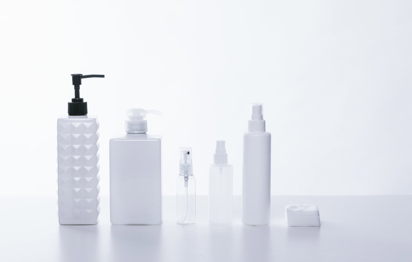 白い背景に並ぶ乳白色と透明なコスメ用ボトルや容器