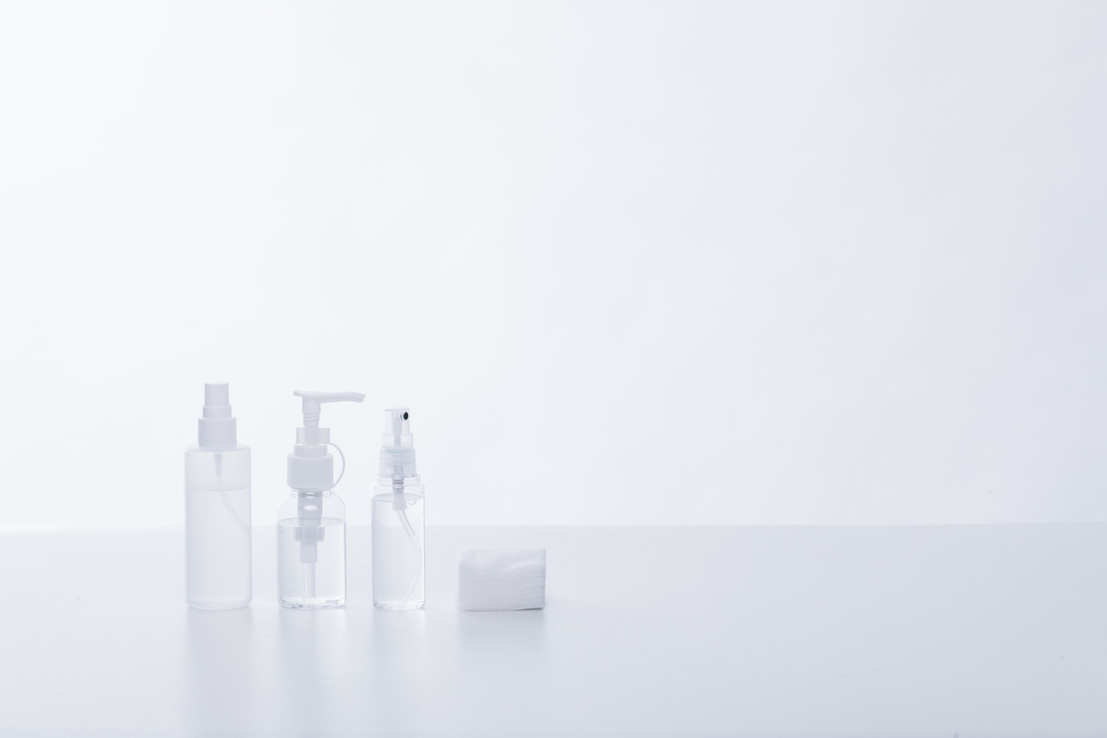 白背景に配置された透明なスキンケア容器とコットンパッド