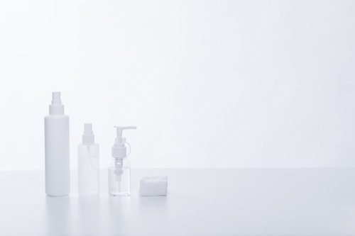 白い背景に並べた化粧水ボトルとコットン、スキンケア用品