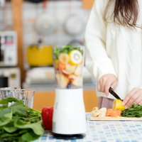 キッチンでスムージー用の野菜をカットする女性の写真