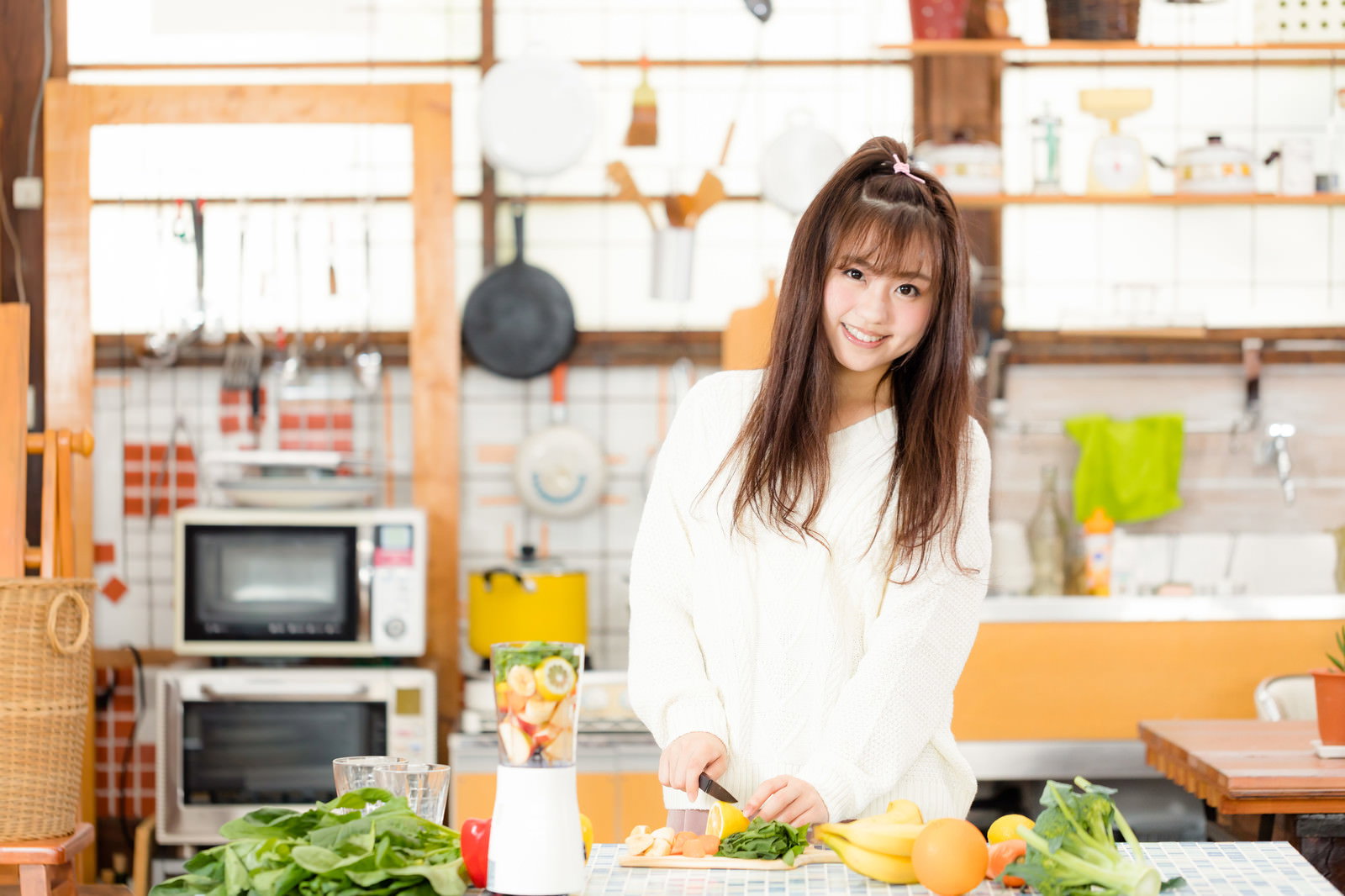 キッチンでスムージーの材料を切る女性［モデル：河村友歌］