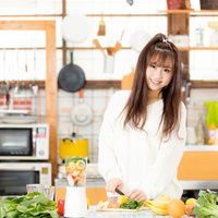 キッチンで新鮮な野菜と果実からスムージーを作る女子の写真