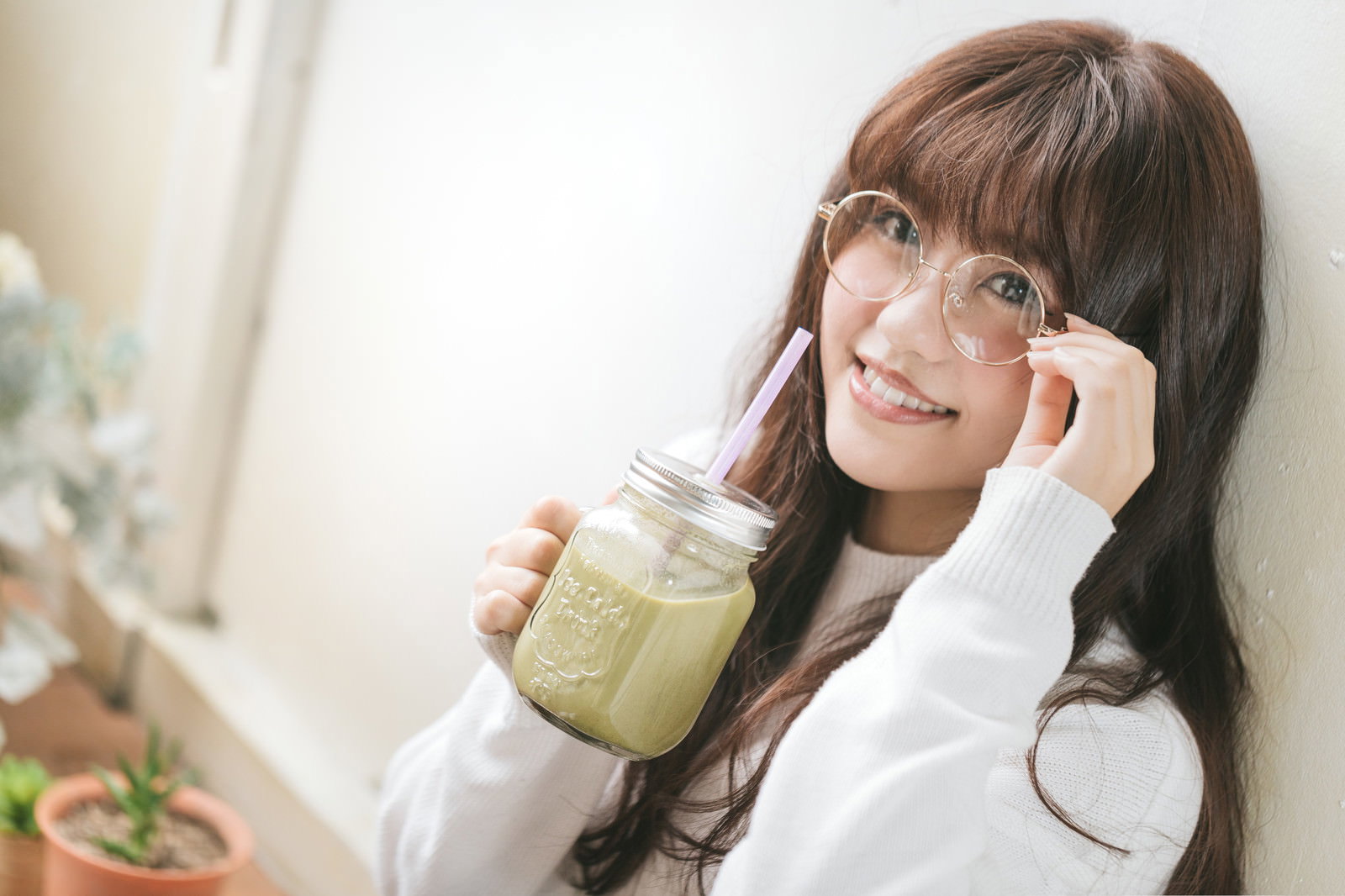 グリーンスムージーを飲もうとする眼鏡をかけた笑顔の女性［モデル：河村友歌］