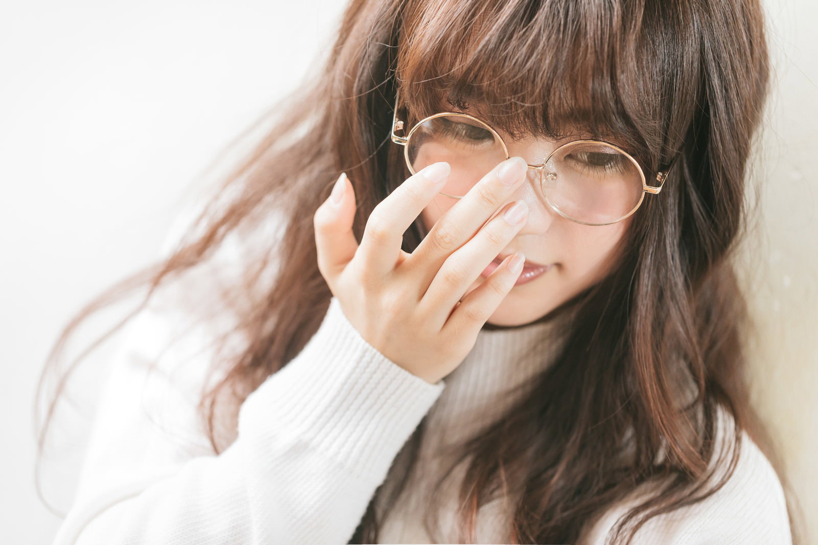 眼鏡をかけた女性が手を顔に当てて考え込んでいる様子［モデル：河村友歌］