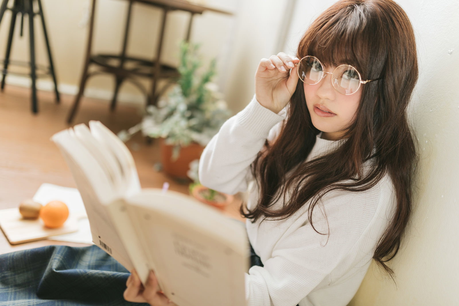 白いニットを着て眼鏡をかけた女性が本を読んでいる［モデル：河村友歌］