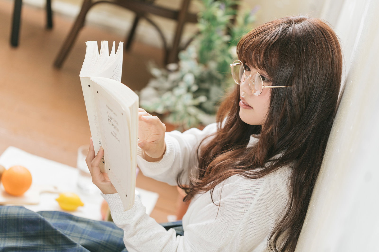 白いトップスを着た眼鏡の女性が本を持ち読書している横顔［モデル：河村友歌］