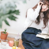 読書しながらグリーンスムージーを楽しむ眼鏡の女性の写真