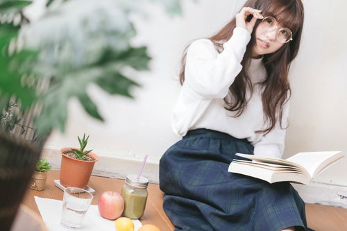 読書しながらグリーンスムージーを楽しむ眼鏡の女性