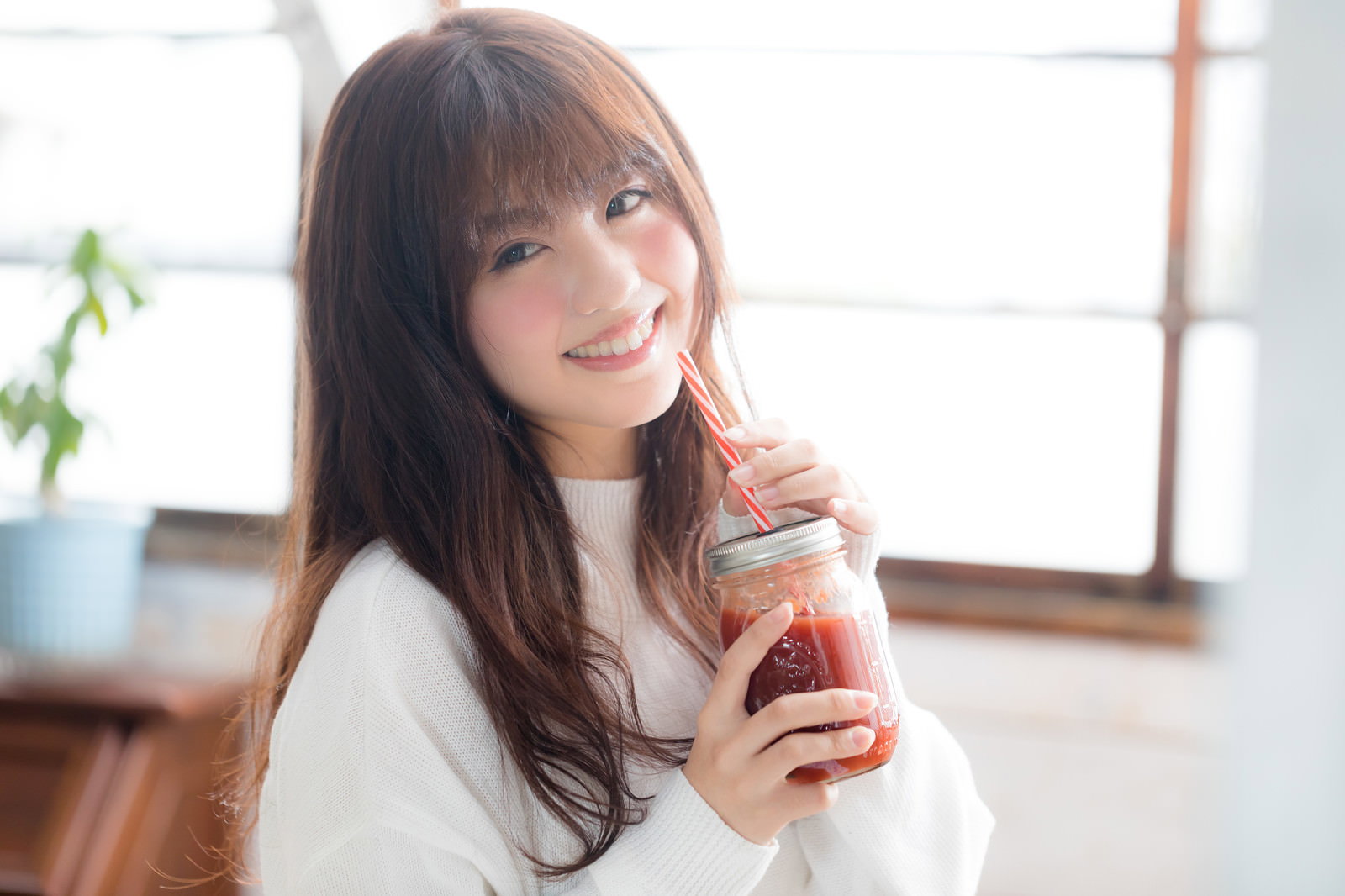 赤いスムージーをストローで飲みながら笑う女性［モデル：河村友歌］