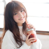 レッドスムージーを飲む笑顔の若い女性のポートレートの写真