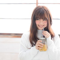 白いセーター姿で笑顔でスムージーを飲む女性の写真