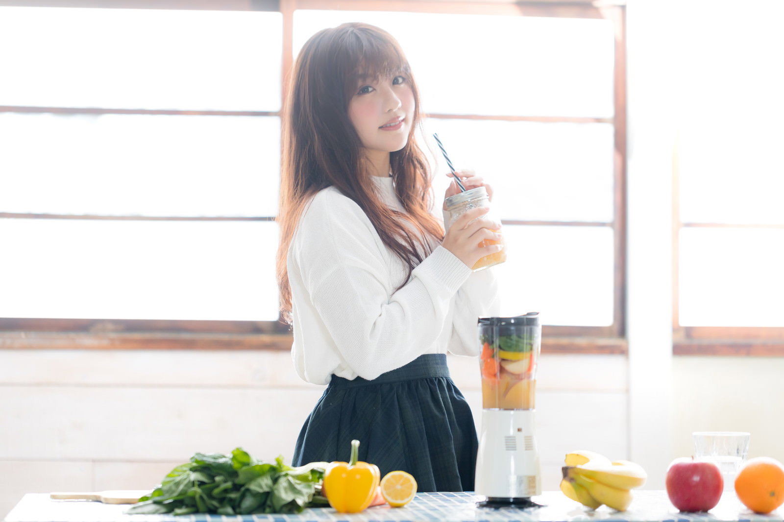 テーブルに並んだ野菜や果実の横で、スムージーを持つ女性［モデル：河村友歌］