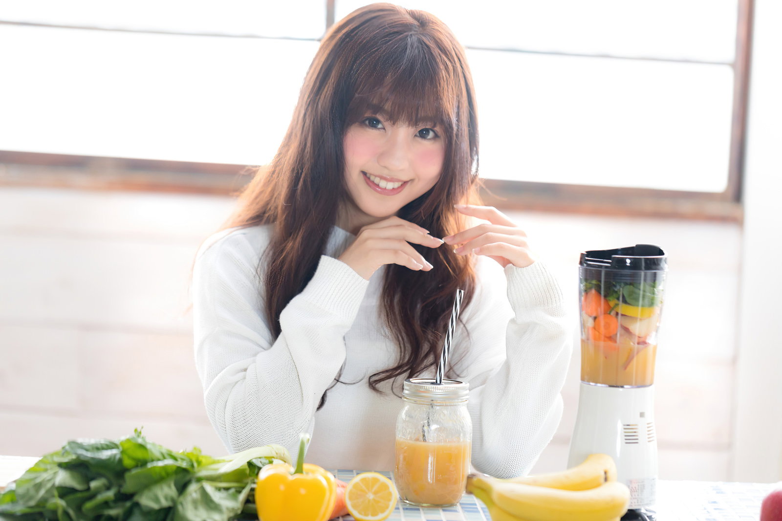 フルーツスムージーを作った女性が笑顔でテーブルに座っている［モデル：河村友歌］