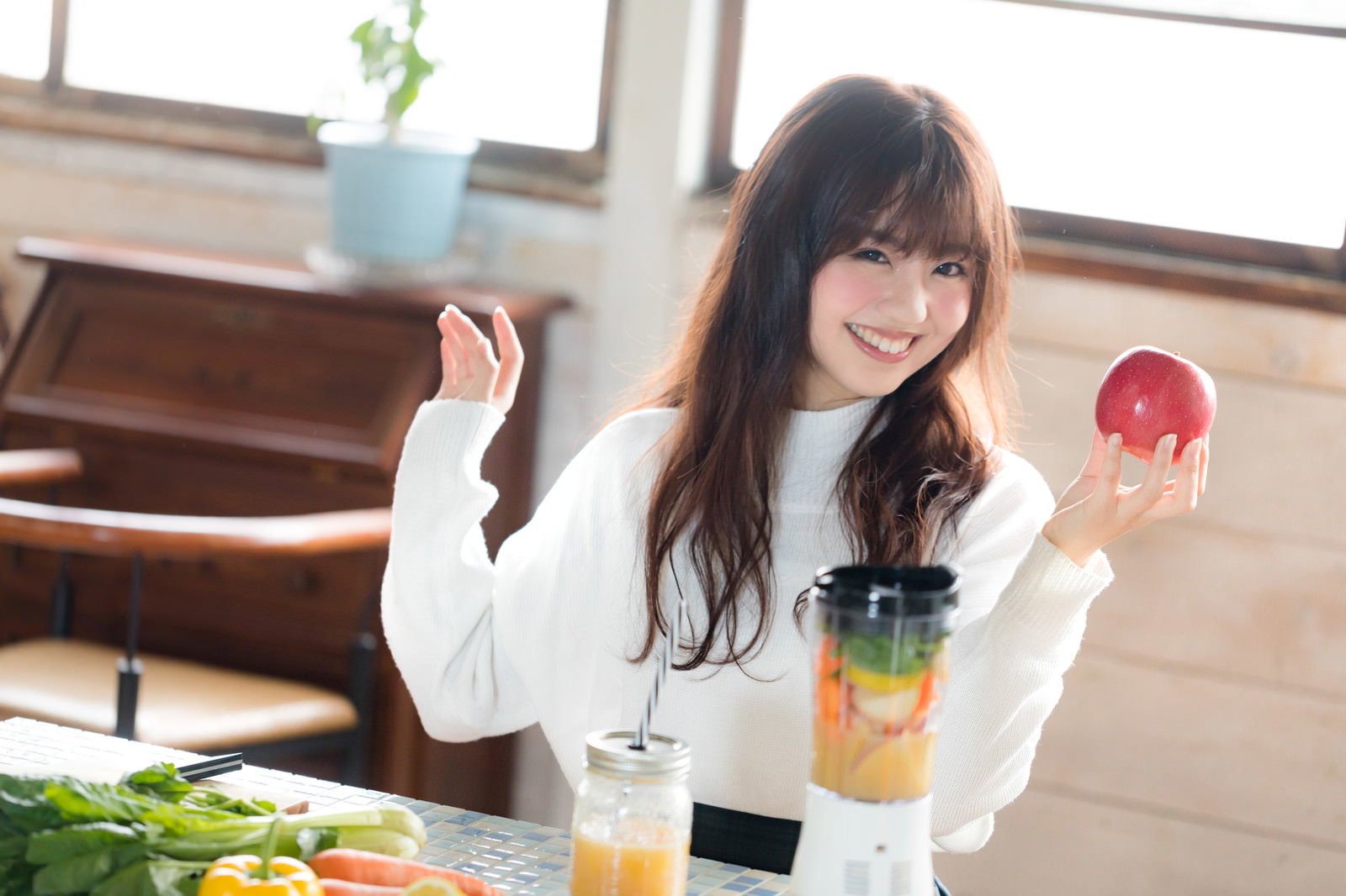 明るい室内で赤いりんごを手に持ち笑顔を見せる女性［モデル：河村友歌］