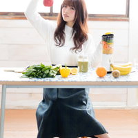 赤いりんごを持ってスムージーにするか迷う女性の写真