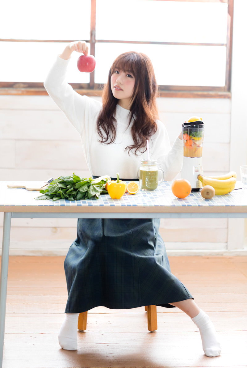 赤いりんごを手に持ち、ジューサーの前で考える女性［モデル：河村友歌］