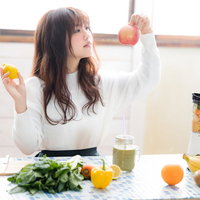 スムージーに入れる果物（リンゴ・レモン）を選ぶ若い女性の写真