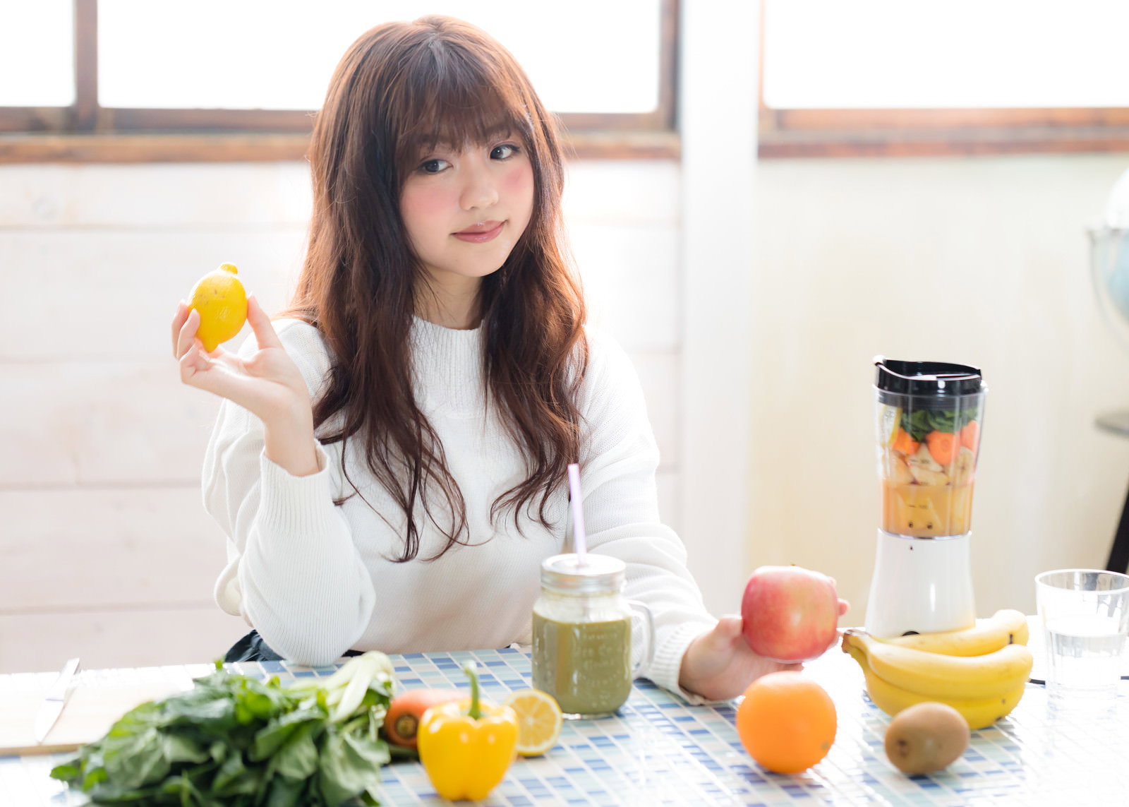 白いテーブルでレモンを手に持って微笑む女性とジューサー［モデル：河村友歌］